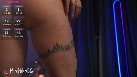 Media: A video of a woman's bare thigh with a tattoo of the word \"SALUD\" partially visible, set against a dark, dimly lit background with a blue neon light.