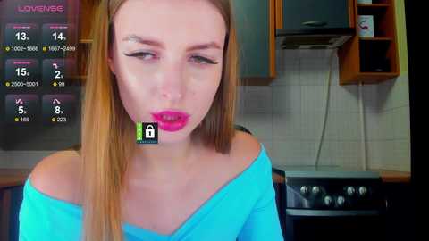 Video of a blonde woman with pink lipstick, wearing a turquoise off-shoulder top, in a modern kitchen with tiled walls, a black oven, and a virtual overlay showing 15% love.