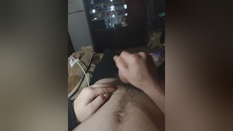 A video of a man's lower abdomen with a visible erection and pubic hair, lying on a bed. In the background, a TV displaying a blurry image of a man's face.