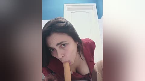 Media: A video of a young woman with long dark hair performing oral sex on a light-skinned, circumcised penis. She is wearing a red top, and the background features a blue wall and white door.