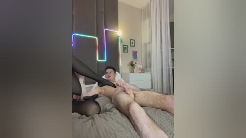 Video of a nude man and woman on a bed, with colorful neon lights in the background.