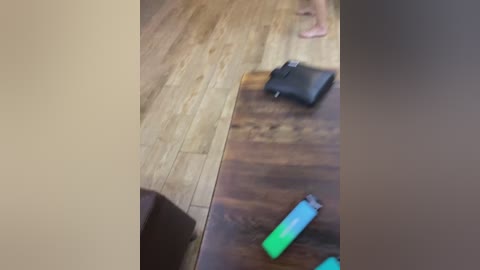 A video of a wooden floor with a black wallet, a green lighter, and a pair of pink shoes visible.
