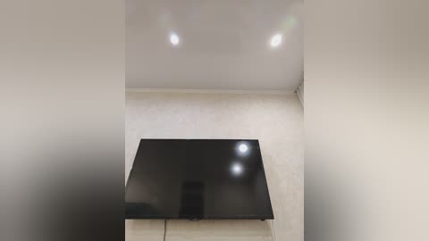 Video of a minimalist room with a sleek, black flat-screen TV mounted on a beige wall, under recessed ceiling lights. The background is plain white, enhancing the modern, clean aesthetic.