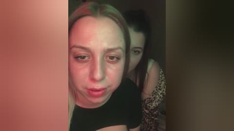 Media: Video of two young women: one with blonde hair and a pouty expression, and the other with dark hair and a leopard print top, both in a dimly lit room.