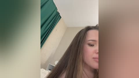 Media: Video of a young woman with long brown hair, fair skin, and closed eyes, standing beside a beige wall with a green curtain.