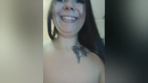 Video of a smiling woman with long dark hair, light skin, and a black feather tattoo on her left shoulder.