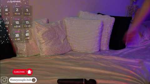 Video of a dimly lit bedroom with white pillows on a bed, a digital calendar displaying 4/10/20, and a TV remote on the bed.
