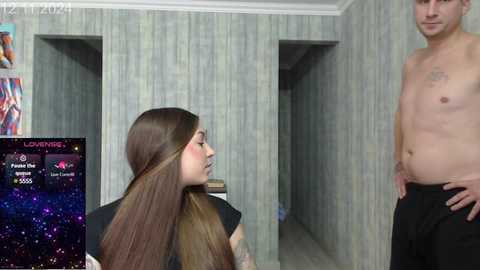 Video of a woman with long brown hair in a salon chair, a tattooed man standing shirtless, and a TV screen displaying \"Loverboy\" in the background.