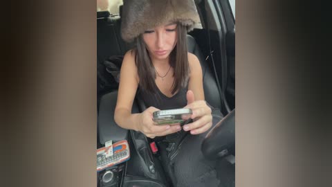 Media: A video of a young woman with a fur hat, wearing a black tank top, holding a smartphone in a car.