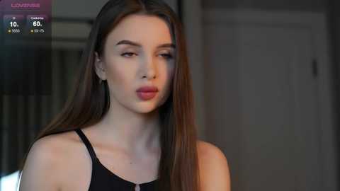 Media: A video of a young woman with long brown hair, fair skin, and red lipstick, wearing a black top, in a dimly lit room with a blurred background.