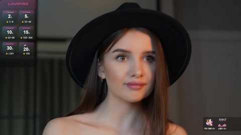 Media: Video of a young woman with fair skin, straight brown hair, and a black hat, looking slightly off-camera, in a dimly lit room with a digital timer in the top left corner.