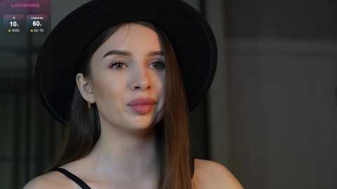 Media: Video of a young woman with long brown hair, wearing a black hat and black top, indoors with dim lighting, displaying a \"Live\" broadcast with a viewer count.