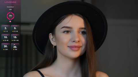 Media: Video of a young woman with fair skin, straight brown hair, and brown eyes, wearing a black hat and black top, smiling softly.