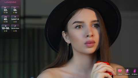 Media: Video of a young woman with long brown hair, wearing a black hat and red lipstick, looking serious.