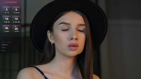 Media: Video of a young woman with long dark hair, wearing a black hat and a black top, with a weather forecast overlay in the background.