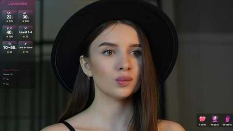 Media: Video of a young woman with long, straight dark hair, wearing a black hat and black top. Background shows a virtual reality game interface.