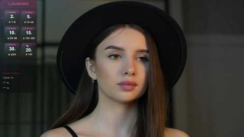 Media: Video of a young woman with fair skin, long dark hair, and a black hat, standing indoors with a blurred background. Weather forecast displayed on the left.