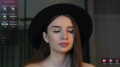 Media: Video of a young woman with fair skin, brown hair, and a black hat, set against a blurred background. She appears serene with closed eyes, looking slightly to the left.