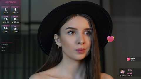 Media: Video of a young woman with long, straight dark hair, wearing a black hat and pink heart filter, set against a blurred, modern indoor background.