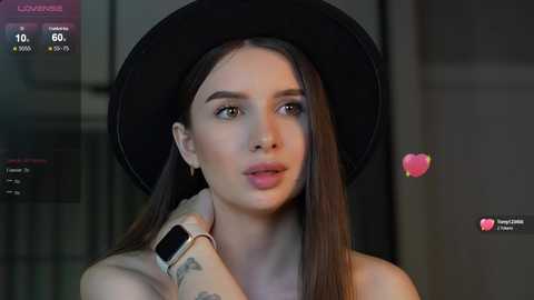 Media: Video of a young woman with long brown hair, wearing a black hat, black top, and a smartwatch, against a blurred background.