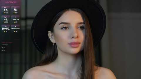 Media: Video of a young woman with long, straight brown hair, wearing a black hat and light makeup. Background shows a dark, blurred interior.