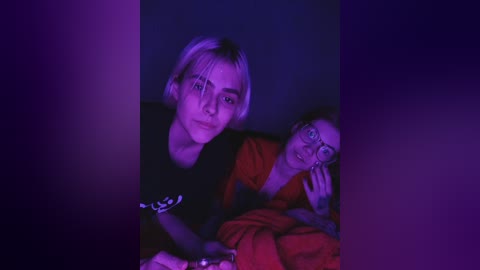 A video of two people, a woman with short blonde hair and glasses, and a man with dark hair, both wearing black shirts, under dim purple lighting.