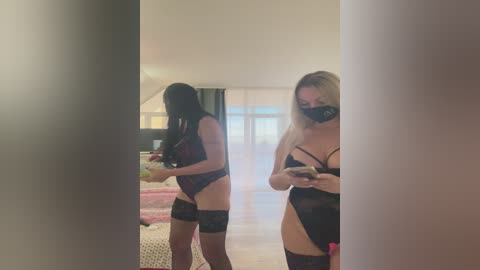 Media: Video of a blonde woman in black lingerie and a face mask, taking a selfie in a dimly lit bedroom with a bed, window, and mirror.