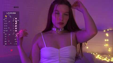 Video of a young woman with long brown hair, wearing a white corset top and black choker, posing against a purple-lit background with fairy lights.