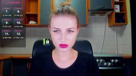 A video of a blonde woman with a bun, wearing a black top, in a modern kitchen with wooden cabinets, tiled backsplash, and a stove.