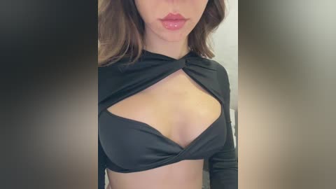 Media: Video of a fair-skinned woman with shoulder-length brown hair, wearing a black, halter-neck top with a large keyhole cutout revealing cleavage. She has full, glossy lips and a neutral expression.