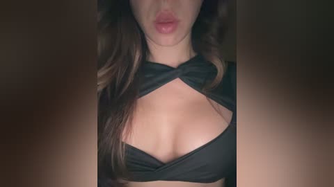 Media: Video of a woman with light skin, wearing a black halter bikini top that reveals ample cleavage, lips slightly parted, with a dark background.