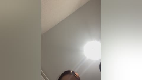 Video of a ceiling with a circular light fixture emitting a bright white light. The ceiling is painted in a light gray color, creating a minimalist and clean aesthetic. The image has a slightly out-of-focus quality.