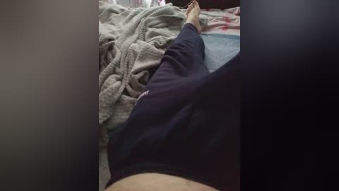 Video of a person lying on a bed, legs crossed, wearing dark pants, light gray blanket, and a red pillow in the background.