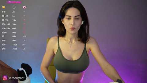 A video of a woman with fair skin, brown hair, and a toned physique, wearing a green sports bra, exercising on a stationary bike in a studio setting.