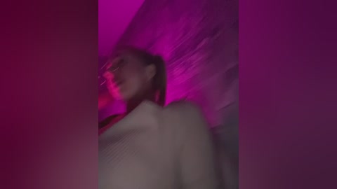 Media: Video of a woman with dark hair, wearing a white sweater, captured in a dimly lit room with purple and pink neon lights creating a moody, trippy atmosphere.