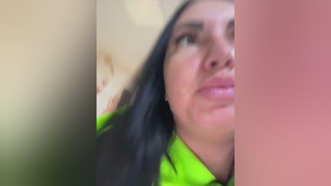 Video of a woman with long black hair, fair skin, and a neon green shirt, partially blurred and out of focus.