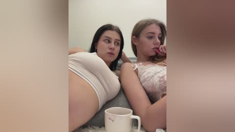 Media: Video of two young women in lingerie, one with large breasts, the other with smaller breasts, lying side by side on a couch.