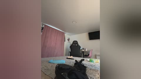 Media: A video of a cozy bedroom with a gaming setup featuring a black gaming chair, a desk with a monitor, and a plush carpet.