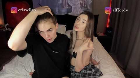 Media: Video of two young women, one topless with a plaid skirt, the other in a black top, in a dimly lit bedroom.