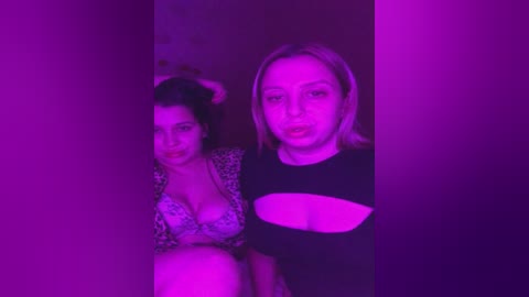 Media: Video of two women in a dark, purple-lit room. One wears a leopard-print bra, the other a black top. Their faces are partially obscured by shadows.