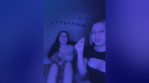 Media: Video of two women in a dimly lit room, one wearing a lace bra and the other a black top. They have fair skin, long hair, and are smiling.