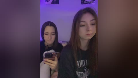 Media: Video of two teenage girls in a dimly lit room, one with long brown hair wearing a Nirvana shirt, the other with short black hair.