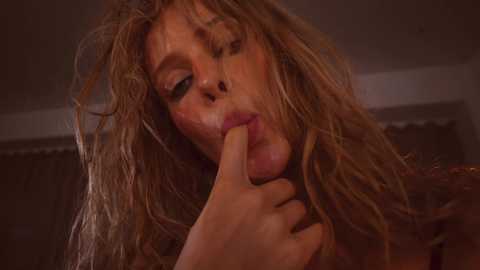 Media: Video of a woman with messy, wet, blonde hair, making a \"V\" with her fingers in her mouth, eyes half-closed, looking seductive.