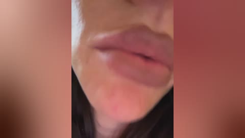 Media: A blurred, close-up video of a person's lips, slightly parted, with a hint of pink lipstick, set against a reddish background. The image is soft-focused, making details difficult to discern.