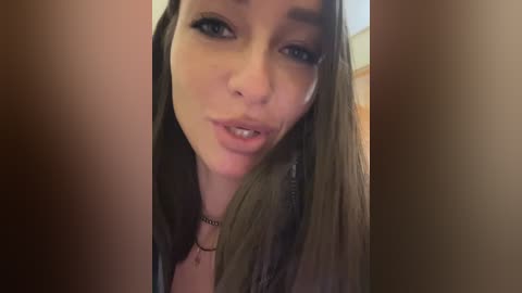 Media: Video of a young woman with long, straight brown hair, light skin, and blue eyes, wearing a black choker necklace, in a dark, blurry background, making a pouty face.
