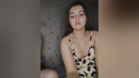 Media: A video of a young Asian woman with long, dark hair, wearing a low-cut leopard-print top, sitting in a dimly lit room with wallpaper featuring abstract patterns.