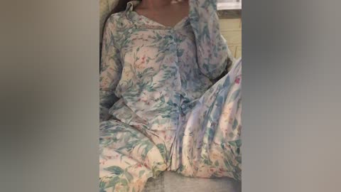 Media: A video of a person in floral pajamas, sitting on a bed, with a blurred background. The pajamas have a pastel color palette with green and blue floral patterns.