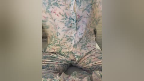 Media: Video of a person wearing a floral-patterned, button-up shirt and matching pants, seated on a wooden floor with a blurred background. The person's posture is relaxed, with their legs spread apart and hands resting on their lap.