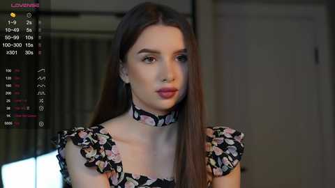 Media: Video of a young woman with long brown hair, fair skin, and a floral-patterned dress, set in a dimly lit room with a clock in the corner.