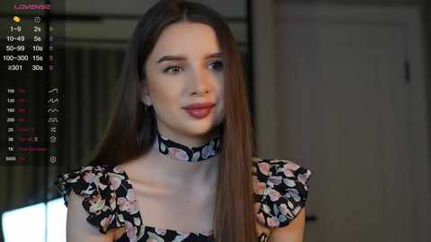 Media: A video of a young woman with long brown hair, wearing a black floral dress with a choker necklace, smiling softly in a dimly lit room.